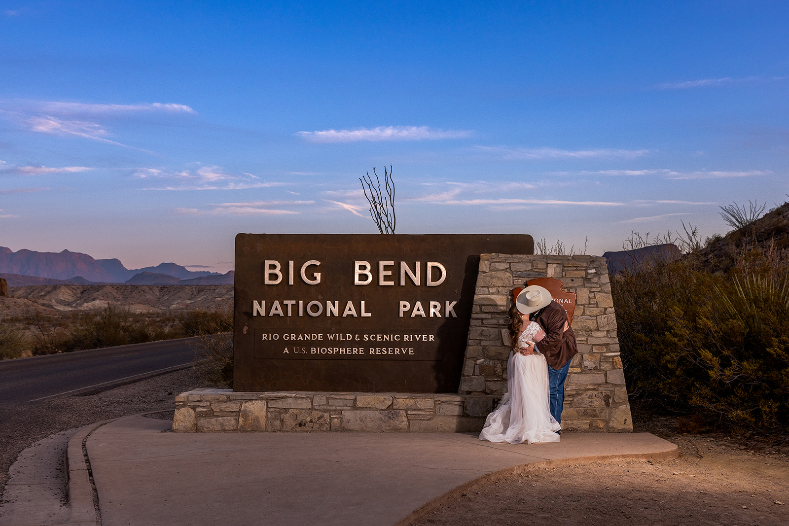 Caitlin and Michael sharing a just married kiss at the entrance to Big Bend National Park during sunset going into blue hour.