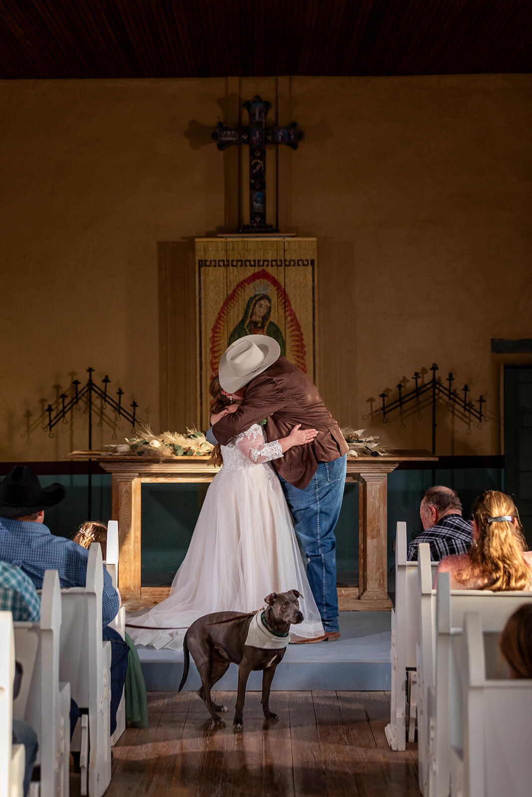 Couple sharing their first kiss inside Saint Agnes Church in Terlingua TX with their friends, family, and pup cheering them on.